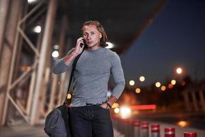 Walking through the street. Man with long hair and travel baggage waiting for the taxi to pick him up photo