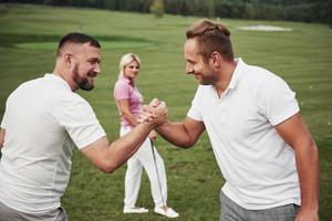 tres jugadores juegan en el campo de golf. el equipo se felicita y se da la mano foto