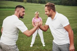 Three players play on the golf course. The team congratulates and shakes hands with each other photo