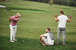 Girl playing golf and hitting by putter on green. Her teacher helps to explore the technique and make her first strikes photo