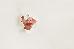 Torn hole in white paper with mouth of young woman with red lips photo