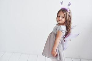 Side photo. Lovely little girl in the fairy costume standing in room with white background photo