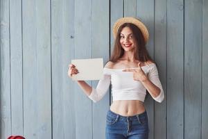 papel vacío en la mano derecha y el índice. mujer joven de pie adentro y sonriendo foto