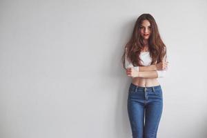 mirada caliente. Hermosa mujer joven sonriente de pie con las manos cruzadas apoyada contra la pared foto