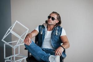 Thoughtful look. Portrait of young fashionable man with sunglasses on grey background photo