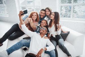 haciendo selfie. Alegres jóvenes amigos divirtiéndose y bebiendo en el interior blanco foto