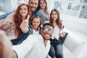 pulgar arriba. Alegres jóvenes amigos divirtiéndose y bebiendo en el interior blanco foto