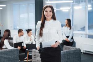 Business and success conception. Portrait of young girl stands in the office with employees at background photo