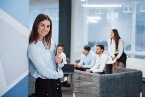 Beautiful modern interior. Portrait of young girl stands in the office with employees at background