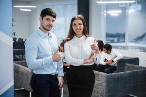 Portrait of two office workers standing in front of employees and showing thumbs up gesture photo