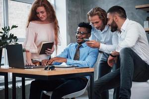 Discussing work using smartphone and laptop. Group of multiracial office workers in formal clothes talking about tasks and plans photo