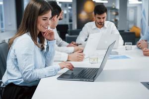 Joy in a job. Side view of girl works on the silver colored laptop in the office and smiling photo