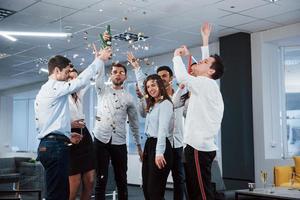 Everyone is happy. Photo of young team in classical clothes celebrating success while holding drinks in the modern good lighted office