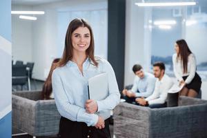 In front of business people. Portrait of young girl stands in the office with employees at background photo