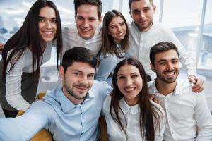 foto del teléfono. Equipo joven haciendo selfie en ropa clásica en la moderna oficina bien iluminada