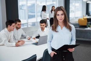 Pretty businesswoman. Portrait of young girl stands in the office with employees at background photo