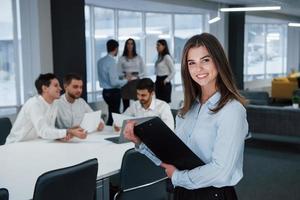 Successful youth. Portrait of young girl stands in the office with employees at background