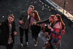 finalmente se conocieron. Vista superior de unos jóvenes amigos que se toman selfie mientras se divierten en el techo con bombillas decorativas de colores foto