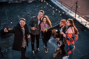 Happy together. Top view of a young friends that take selfie while have fun at the roof with decorative colorful light bulbs photo