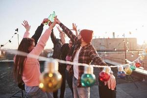 Make a party. Holidays on the rooftop. Cheerful group of friends raised their hands up with alcohol photo