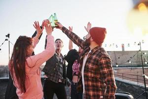 Holidays on the rooftop. Cheerful group of friends raised their hands up with alcohol photo