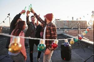 Unity of people. Holidays on the rooftop. Cheerful group of friends raised their hands up with alcohol photo