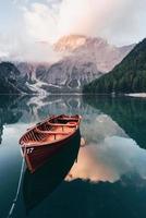 Vertical photo. Wooden boat on the crystal lake with majestic mountain behind. Reflection in the water