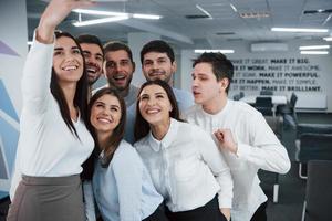 Fooling around fot the camera. Young team making selfie in classical clothes in the modern good lighted office photo