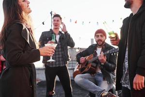 Joyful time. Rooftop party with some alcohol drinking and guitar playing. Sunshine behind photo