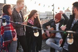 Guy in red hat tells something. Rooftop party with alcohol and acoustic guitar at sunny autumn day photo