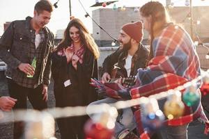 cálido ambiente de amistad entre estos jóvenes hermosos. Fiesta en la azotea con alcohol y guitarra acústica en el soleado día de otoño foto