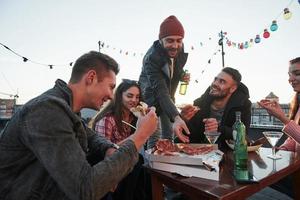 dale una rebanada más. comiendo pizza en la fiesta de la azotea. buenos amigos tienen fin de semana con comida deliciosa y alcohol foto