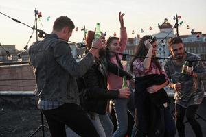 Alcohol in hands. Dancing party on the roof with beautiful sunshine at background. Young stylish people photo