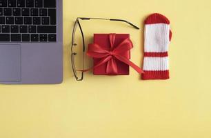 Winter online shopping colored background with Christmas gift box, mitten, glasses, computer keyboard with copy space photo