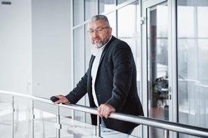 Looking into the camera. Man in classic wear stands in modern building and leaned on the railing photo