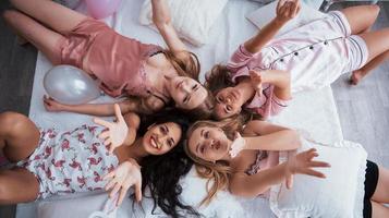 Holidays conception. Top view of young girls at bachelorette party lying on the sofa and raising their hands up photo