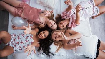 Air kisses. Top view of young girls at bachelorette party lying on the sofa and raising their hands up photo