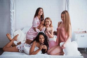 Good food creates nice mood. Cute girls have meeting and holiday in the awesome lighted room with white walls and bed. Chocolate cookies in the hands photo