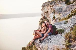 Good mood. Young couple resting from walking at the edge of the mountain. Wonders how far other coast is it photo