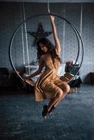 Hanging chair looks great. Pretty woman in golden colored dress sits on the stylish circle shaped bench on the chain. Luxury room photo