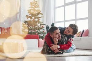 hermosa iluminación y gran ambiente. Encantadora pareja joven tumbado en la sala de estar con árbol de Navidad verde en el fondo foto
