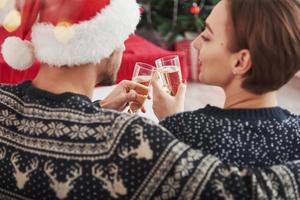 Celebrating new year. Knocking glasses. Beautiful couple in holiday clothes sits and hugs each other. Photo from the back