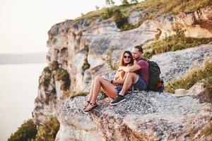 posa para la foto. pareja joven descansando de caminar al borde de la montaña. se pregunta qué tan lejos está la otra costa foto