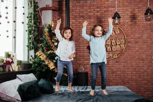 Hands up. Photo of the motion. Cheerful kids having fun and jumping on the bed with decorative holiday background