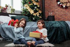 Each one of them have some good present. Christmas holidays with gifts for these two kids that sitting indoors in the nice room near the bed photo