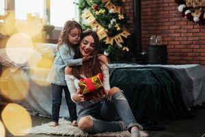 mira lo que tengo para ti. madre e hija se sienta en la habitación decorada de vacaciones y tiene caja de regalo foto