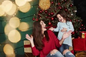 Beautiful mother playing with her daughter in the gorgeous decorated room with Christmass tree photo