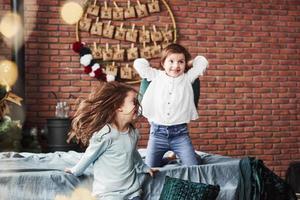 Kid jumping off the sofa. Little girls having fun on the bed with holiday interior at the background photo