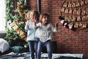 Picture in motion. Cheerful kids having fun and jumping on the bed with decorative holiday background photo
