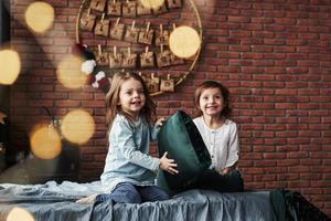 Playing with pillow. Little girls having fun on the bed with holiday interior at the background photo